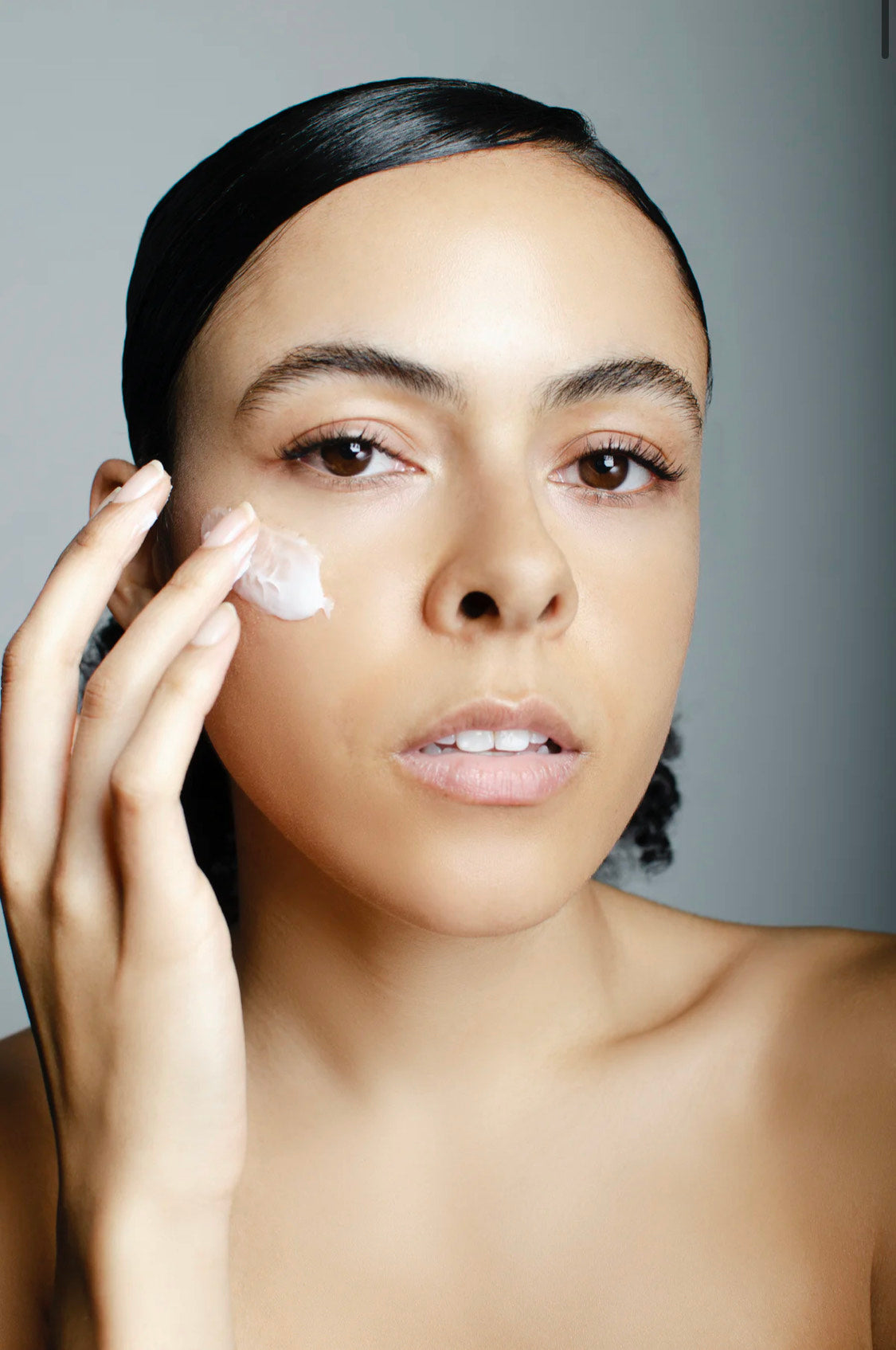 Woman smearing Intrigue Skin face cream on her cheekbone.